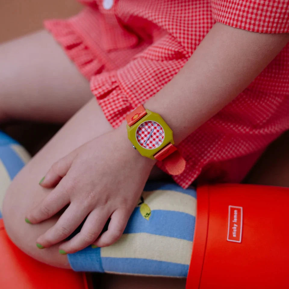 Person wearing a colorful watch with a red and white checkered face, sitting on a striped cushion.