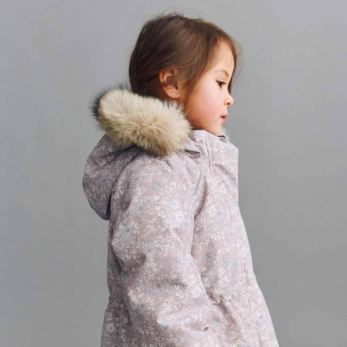 Child wearing a floral coat with a faux fur-lined hood on a gray background