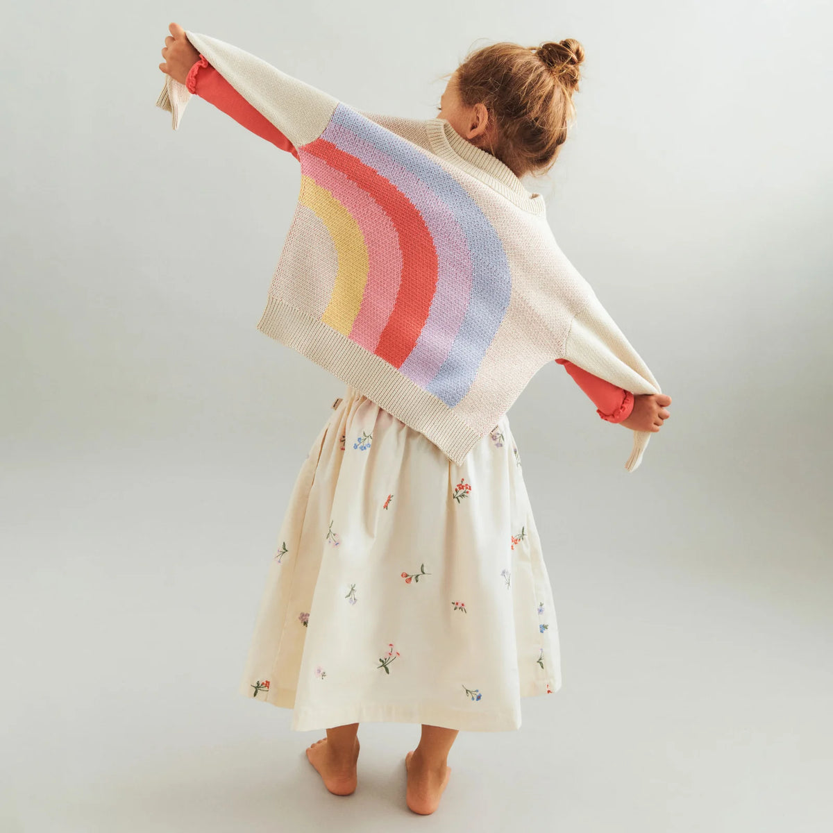 Child wearing a colorful striped sweater over a dress on a plain background