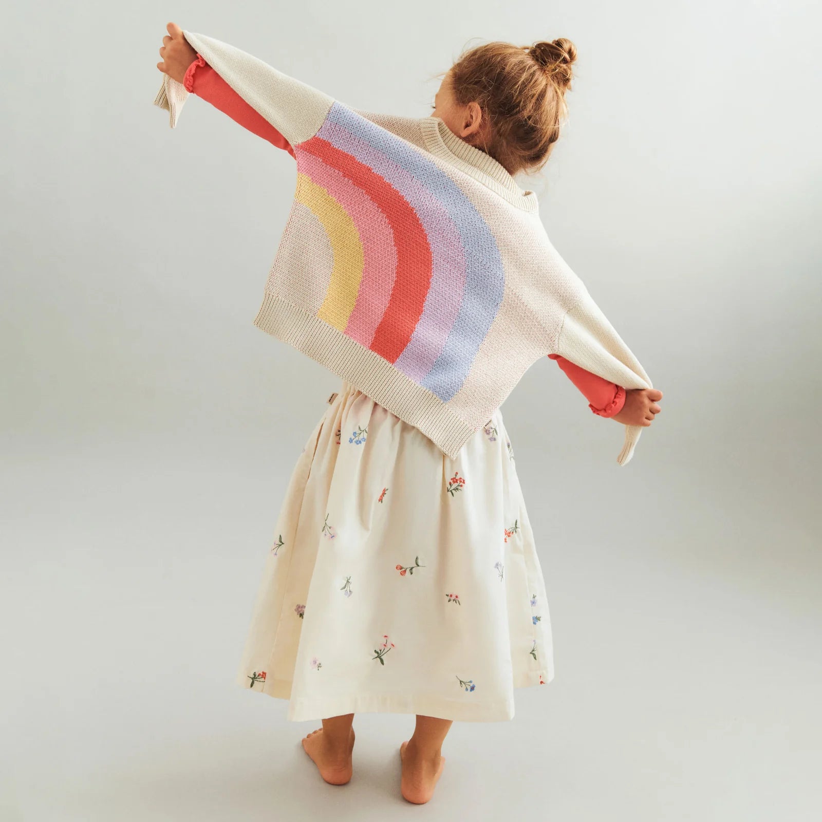 Child wearing a colorful striped sweater over a dress on a plain background