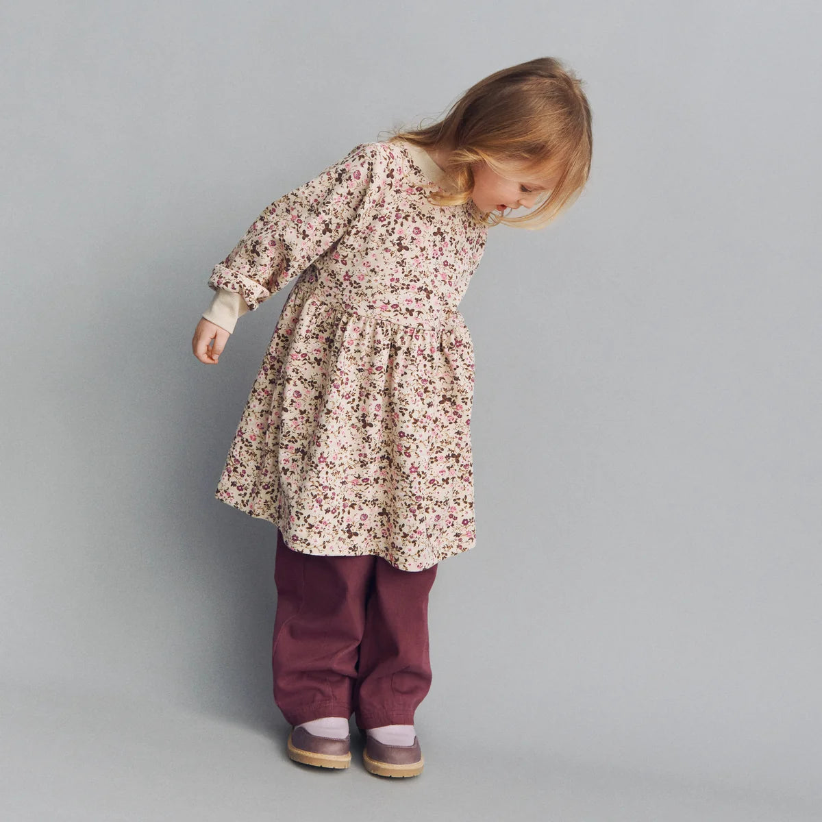 Child wearing a floral dress and purple pants on a gray background