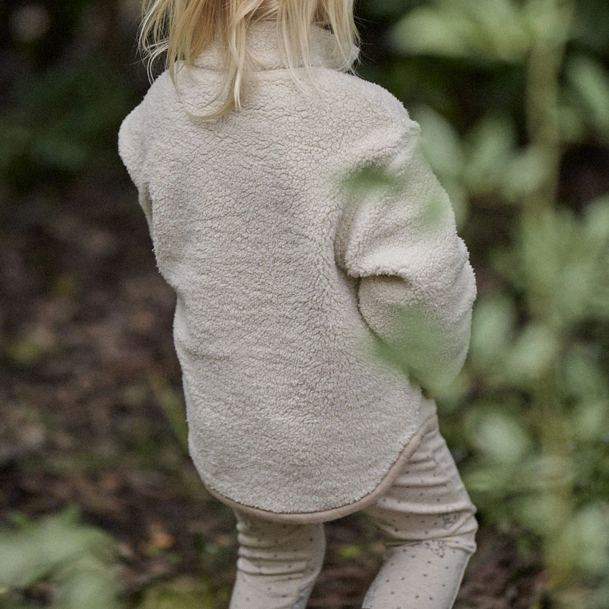 Child wearing a beige fleece jacket in a natural setting