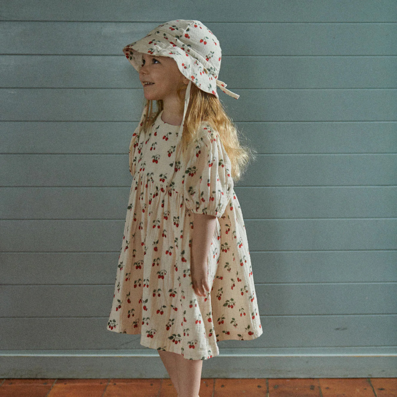 Baby in floral outfit and hat sitting in grass