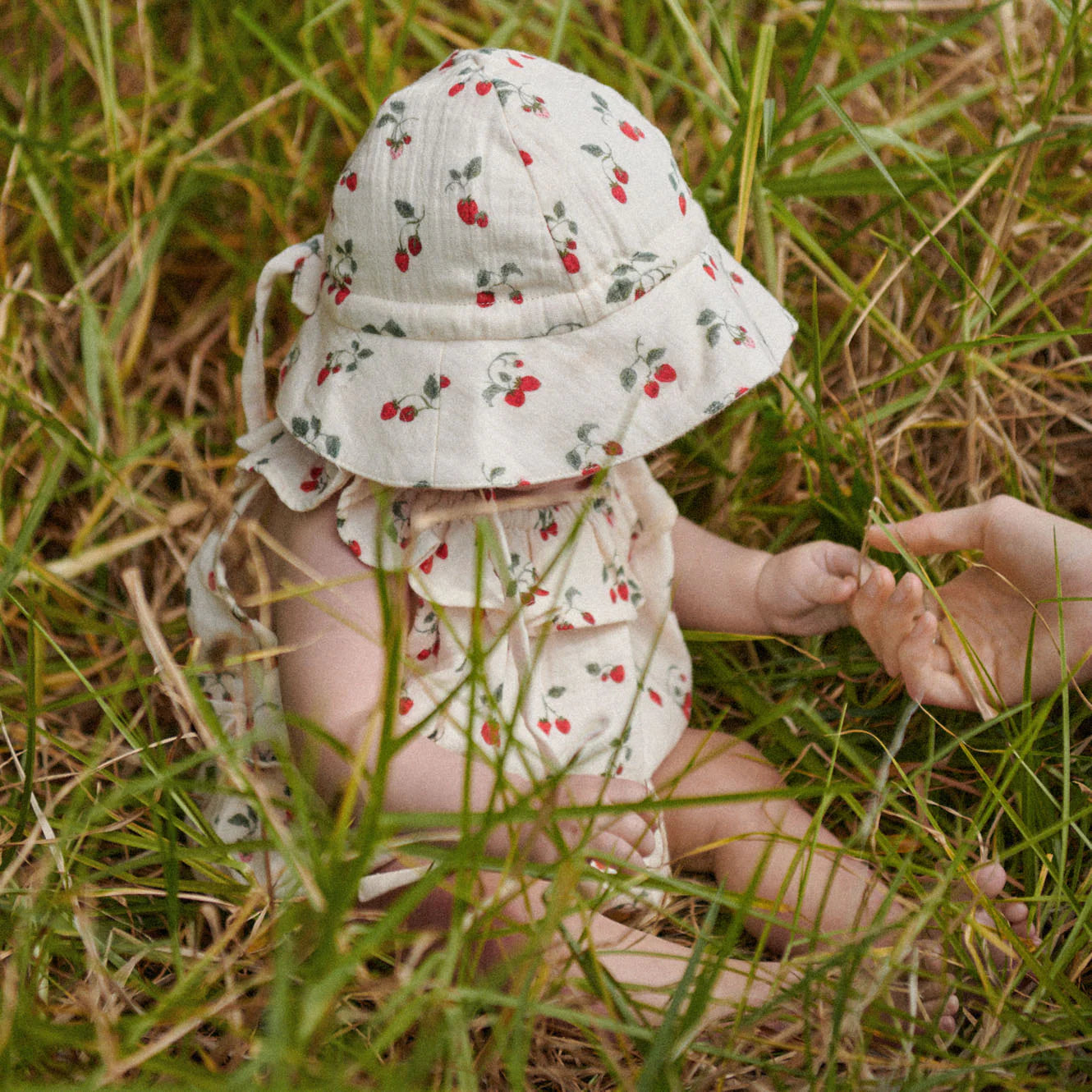 Baby in floral outfit and hat sitting in grass
