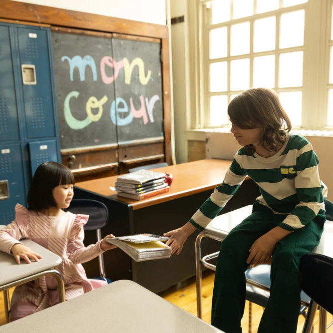 Two kids standing in front of blue lockers in a school hallway.