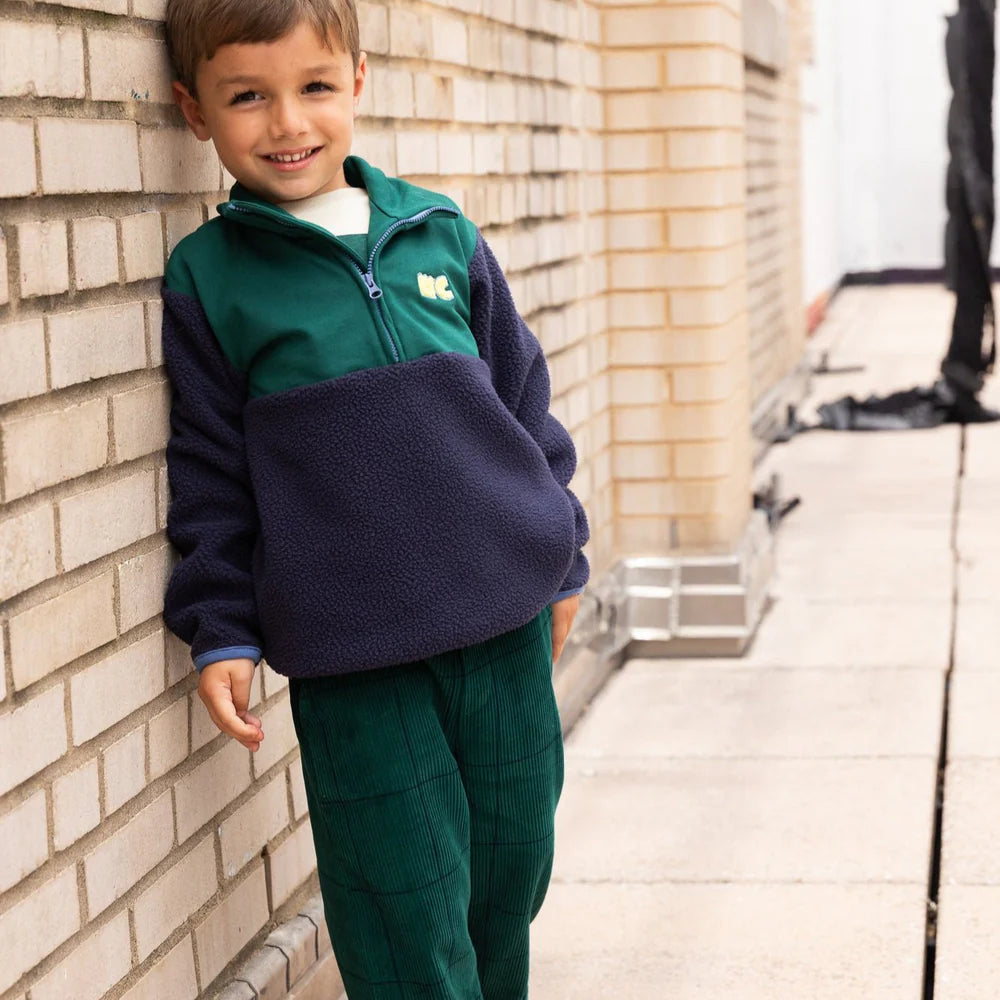Child wearing a green and navy fleece against a brick wall