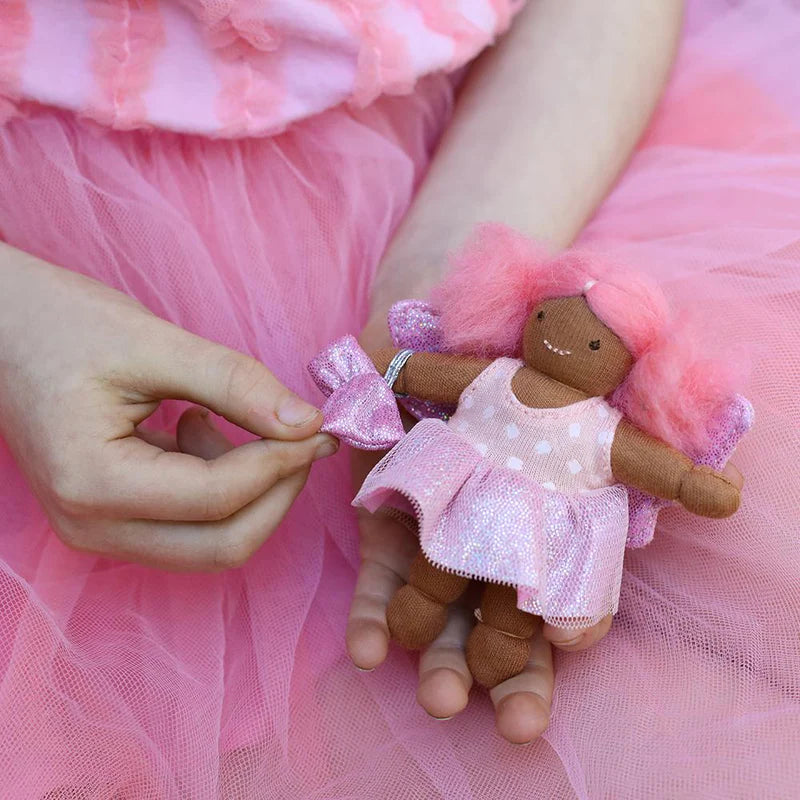 A small doll named Tulip the Tooth Fairy with pink hair, a sparkly fabric skirt, and a tooth-print top, being held by a person.