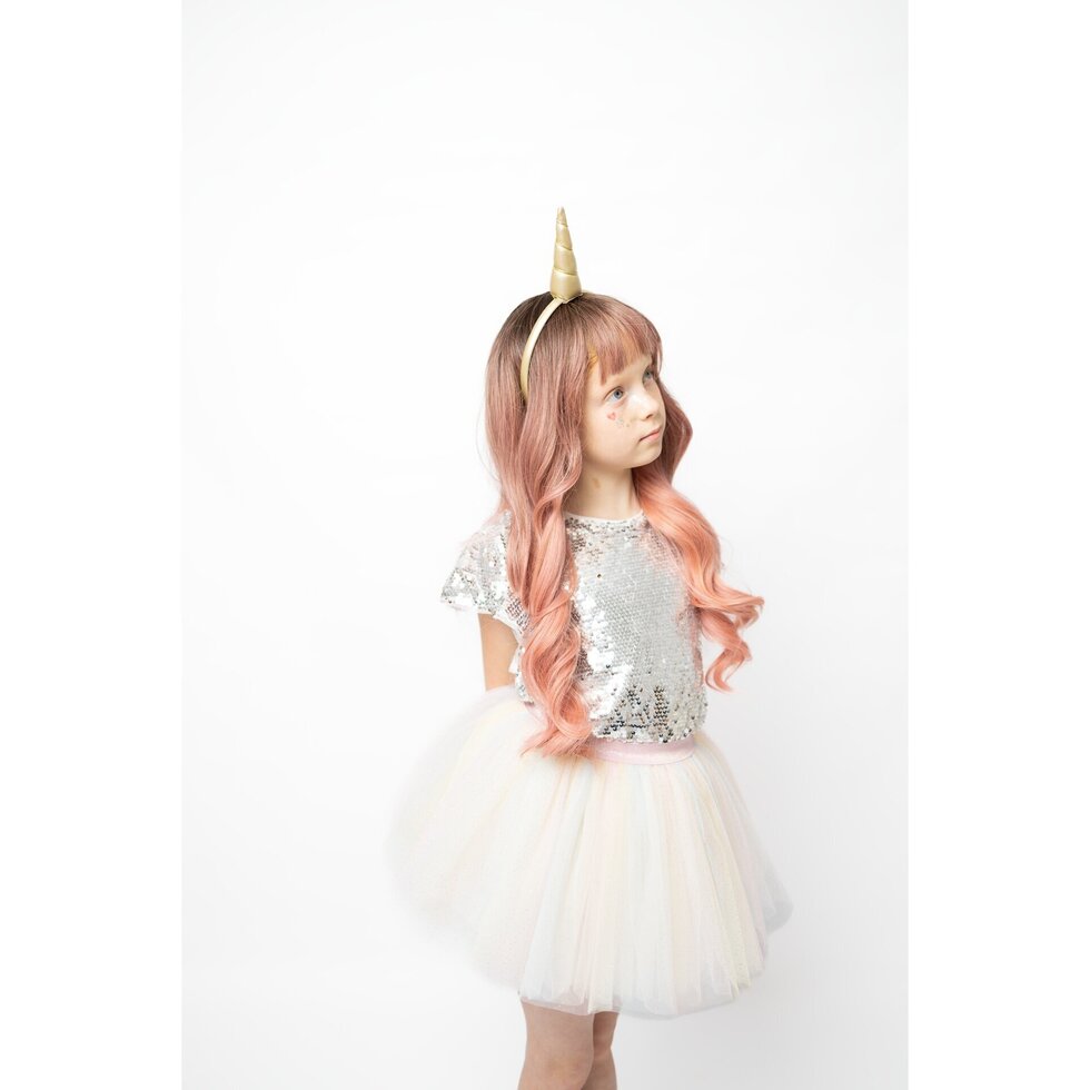 A young girl with long, wavy pink hair wearing a unicorn costume, featuring a silver sequined top, a white tulle skirt, and a gold horn headband, photographed against a plain white background.