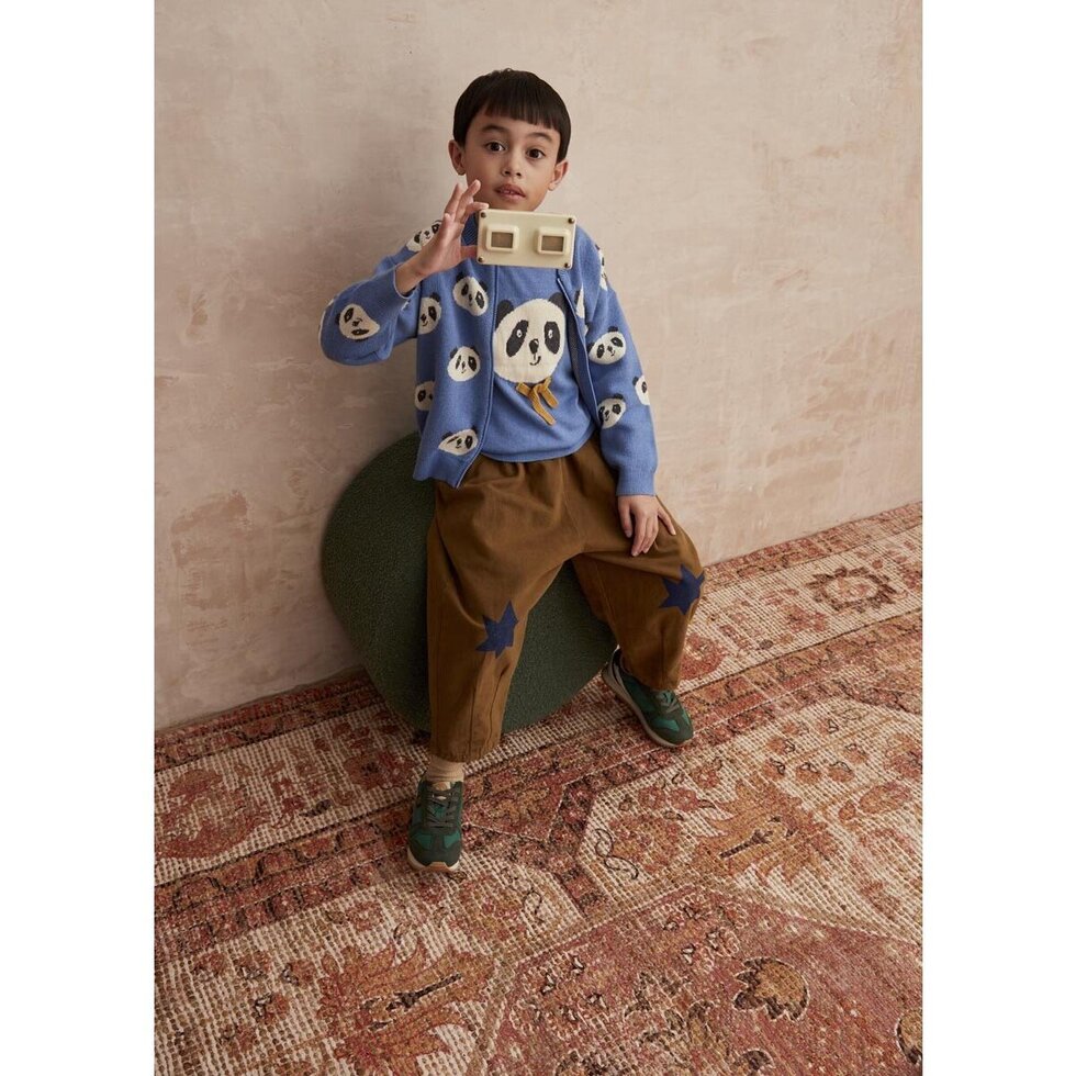 Child wearing a blue sweater with panda designs, sitting on a green chair against a beige wall.