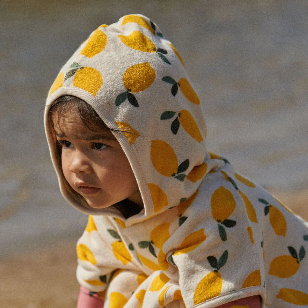 Child wearing a hoodie with lemon pattern on a beach