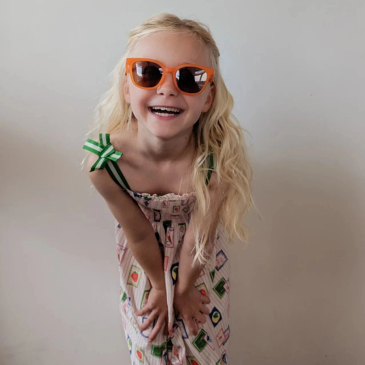 Child wearing orange sunglasses and a patterned dress against a plain background