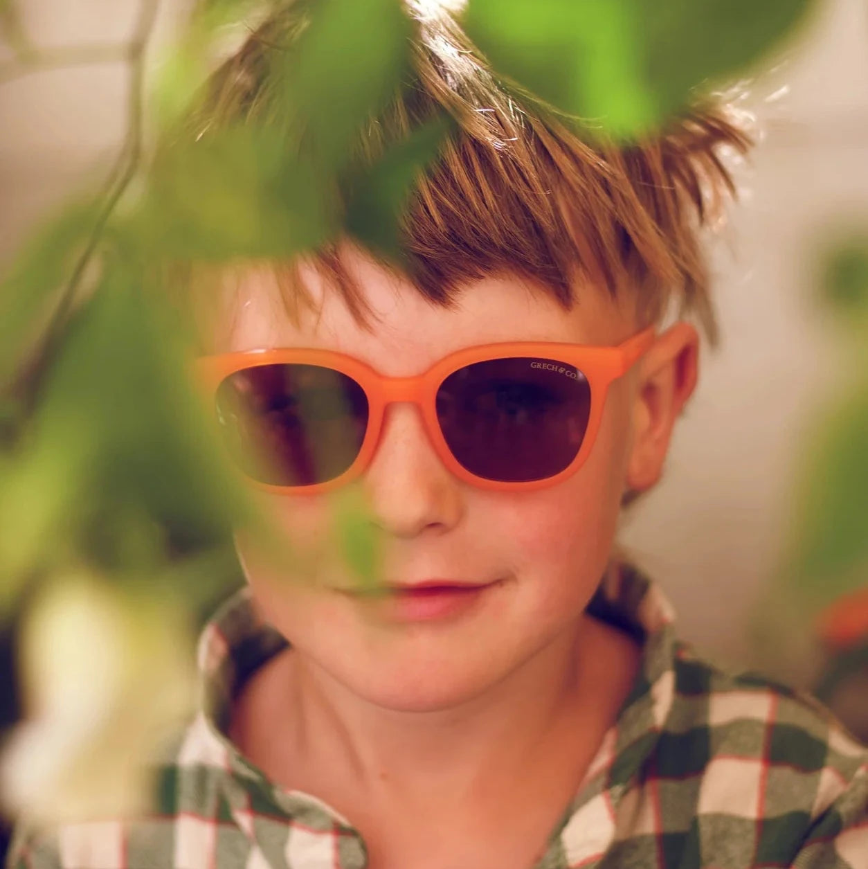 Child wearing orange sunglasses and a patterned dress against a plain background