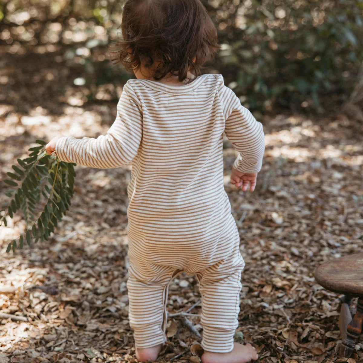 Child in a striped onesie walking outdoors with leaves in hand