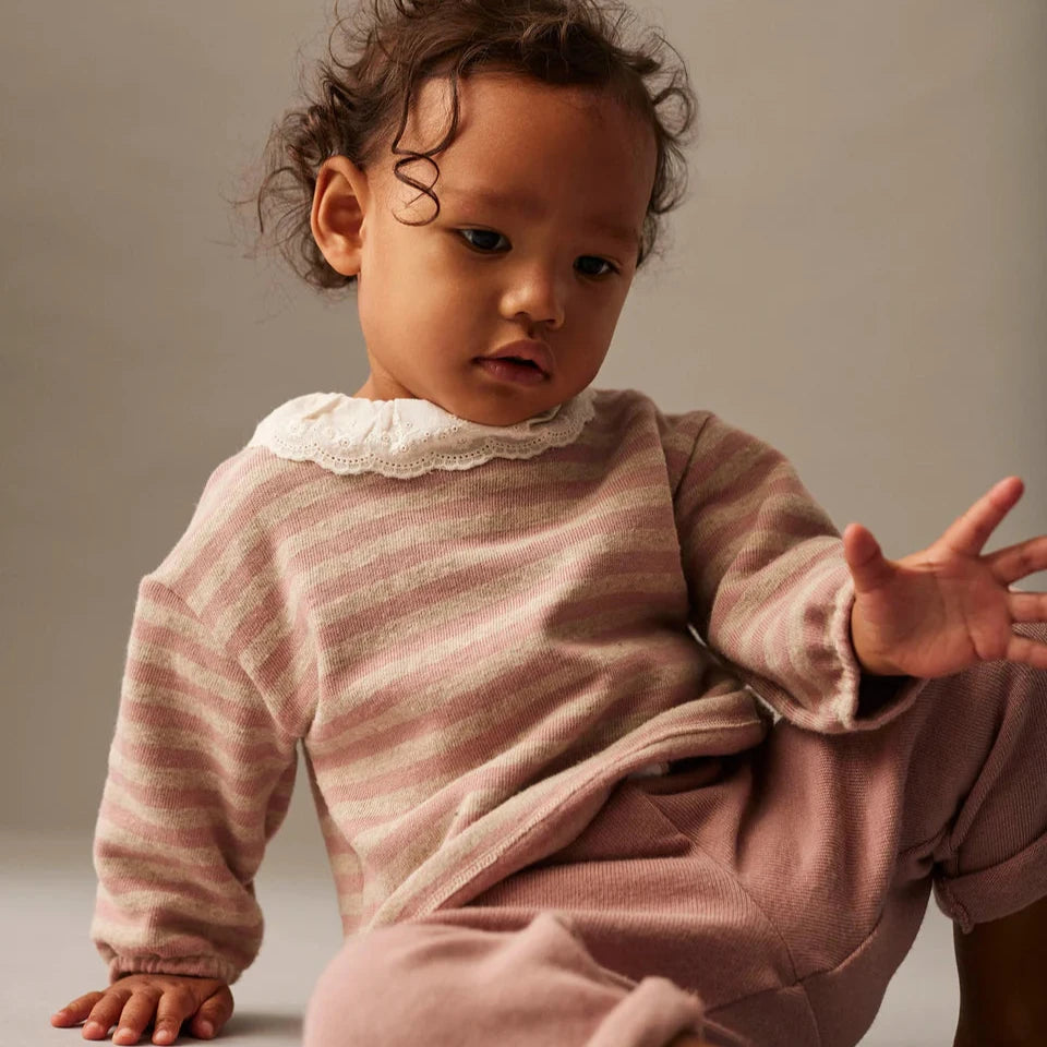 Baby in a pink outfit sitting on a gray surface with a neutral background
