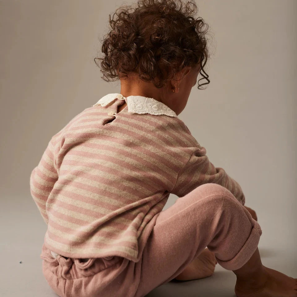 Baby in a pink outfit sitting on a gray surface with a neutral background