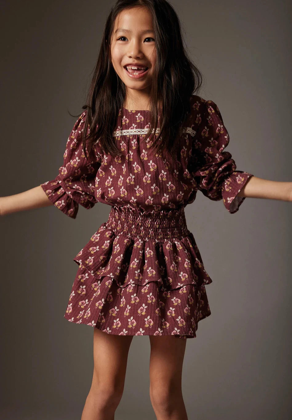 Young girl wearing a maroon floral skirt against a gray background