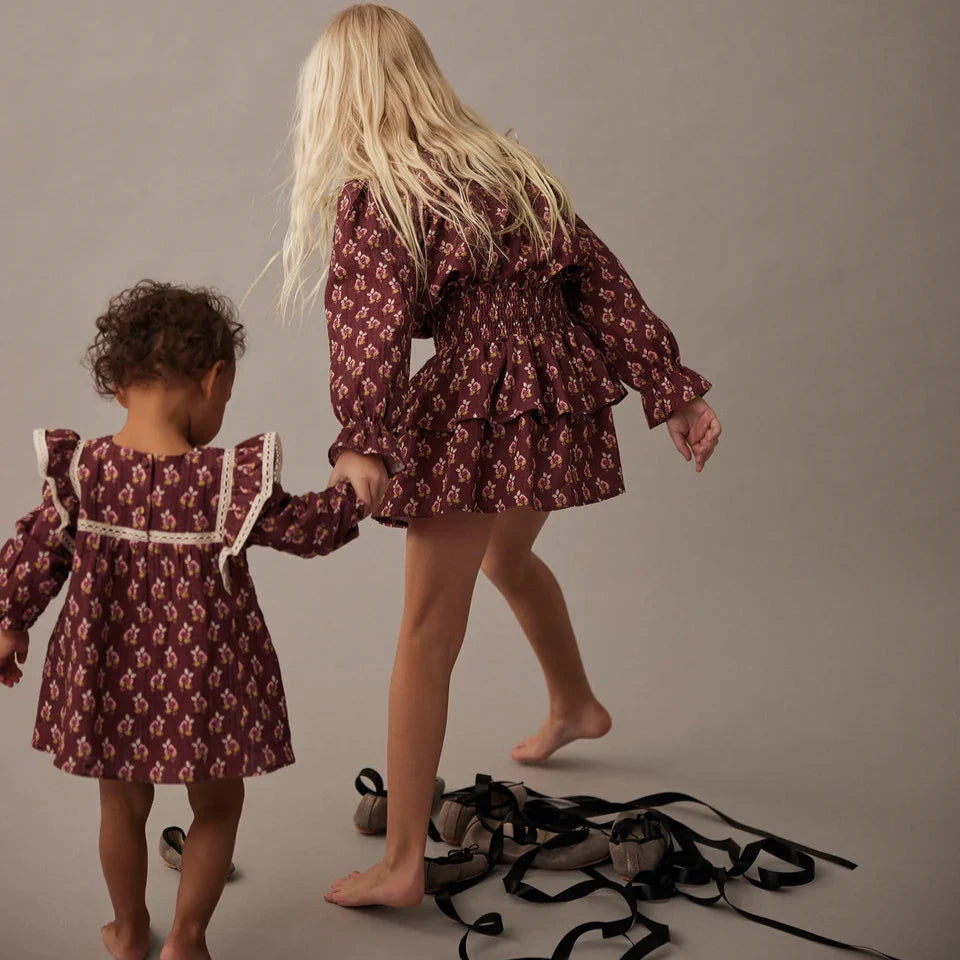 Two children in matching patterned dresses holding hands on a plain background