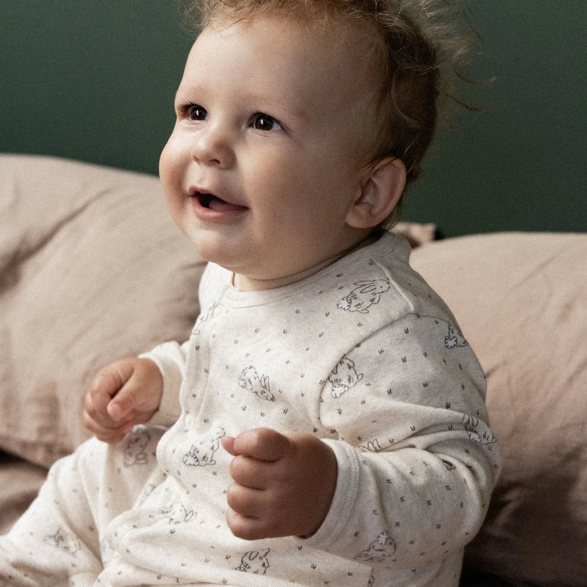 Baby in a patterned outfit sitting on a couch with a neutral background