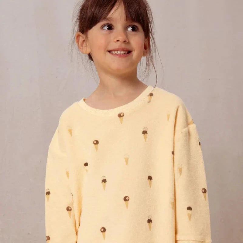 Child wearing a yellow outfit with ice cream cone patterns on a plain background