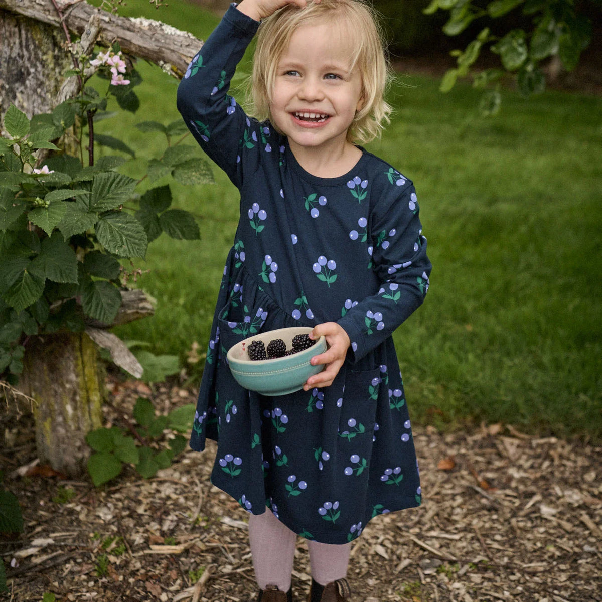 Young girl in a garden holding a bowl of blackberries