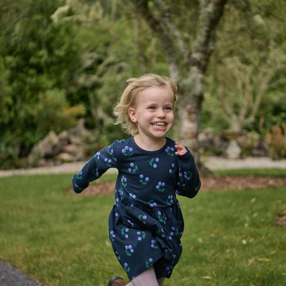 Child in a dark blue dress with a pattern of small shapes running outdoors.