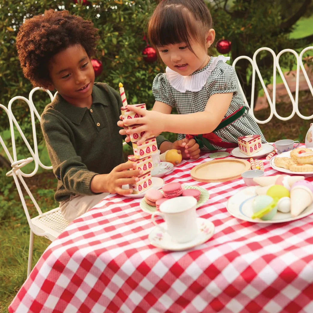 Two children at a picnic table with a red and white checkered tablecloth, surrounded by cake and decorations.