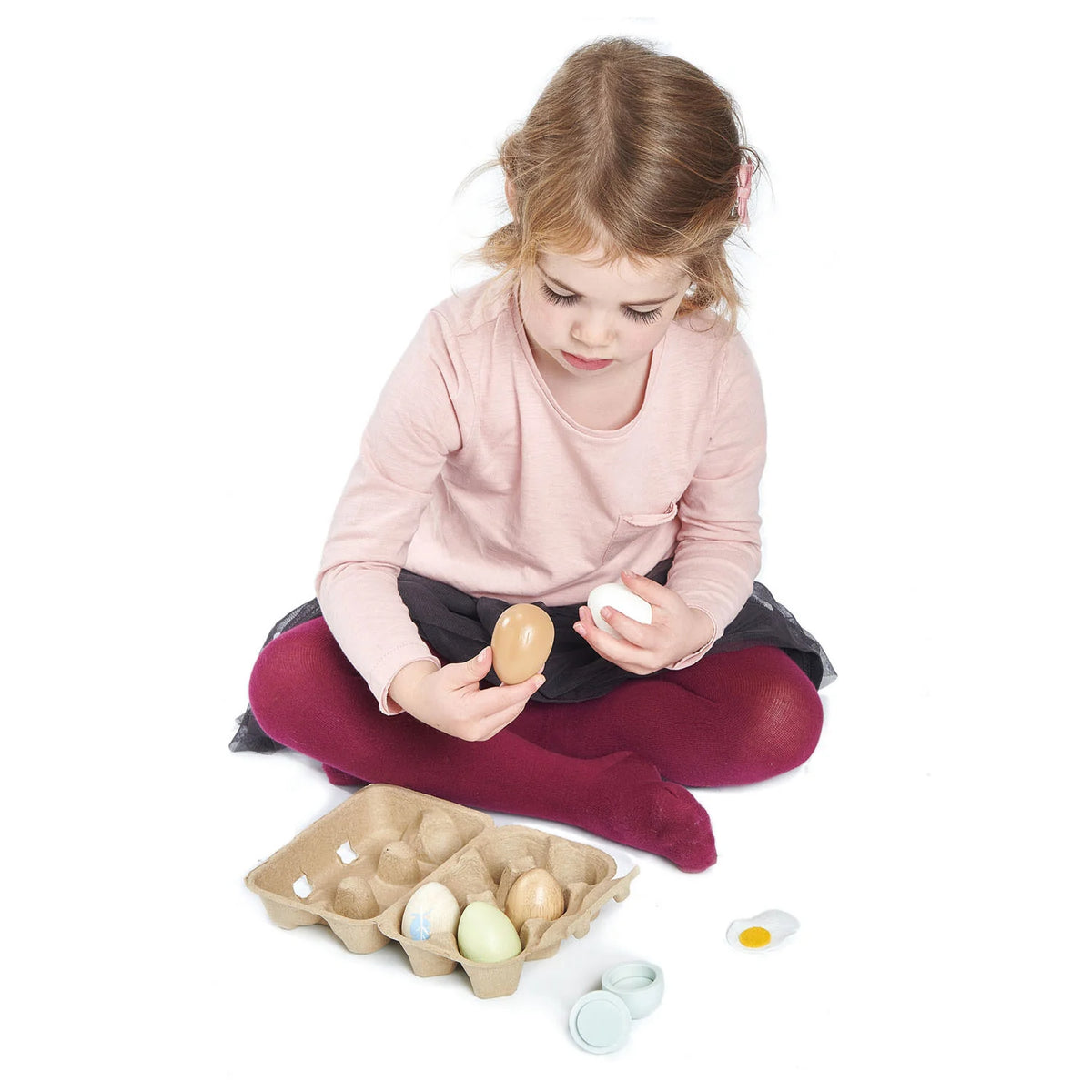 Child playing with wooden eggs and a cardboard egg carton on a white background