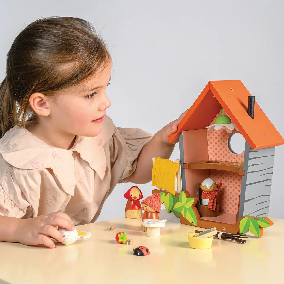 Child playing with a toy house and accessories on a table.