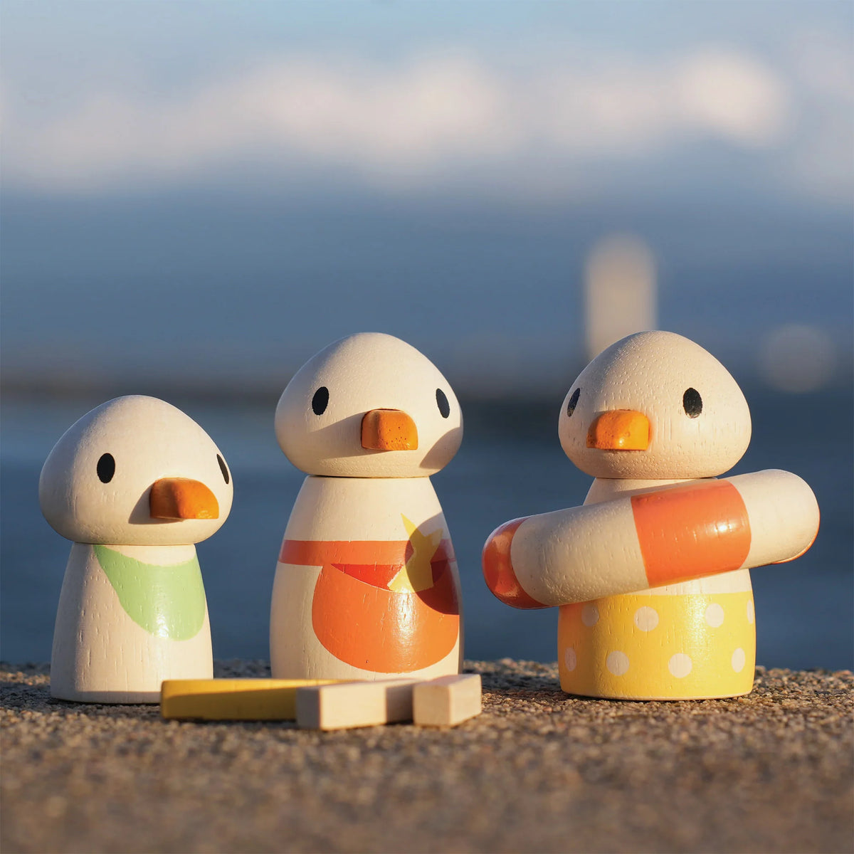 Three wooden duck toys on a beach with a blurred ocean background