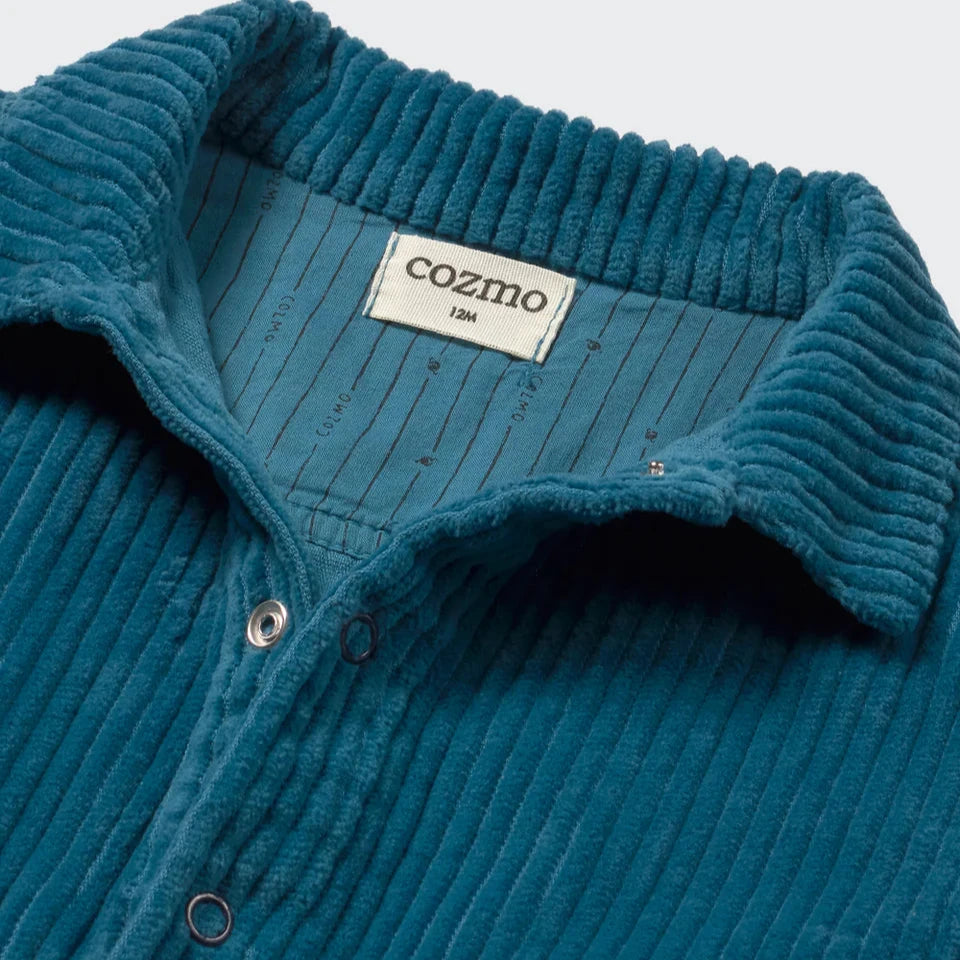 Close-up of a blue ribbed romper with &#39;cozmo&#39; label on a light blue background