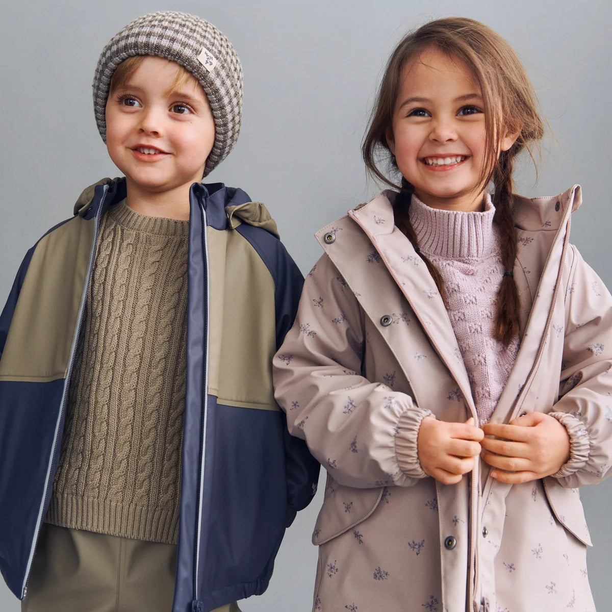 A children's hooded raincoat in a dusty pink color, decorated with a small all-over pattern, shown against a light gray background.