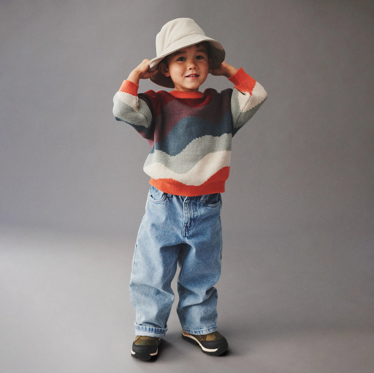 Child wearing a colorful striped sweater and jeans against a gray background
