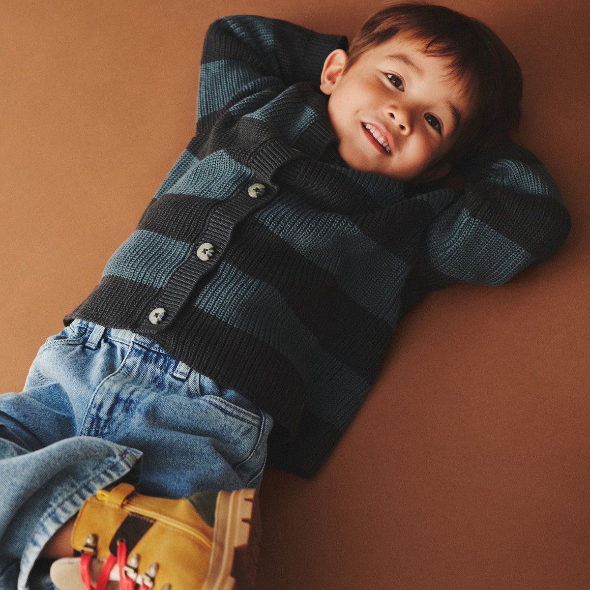 Child wearing a striped sweater and jeans against a brown background