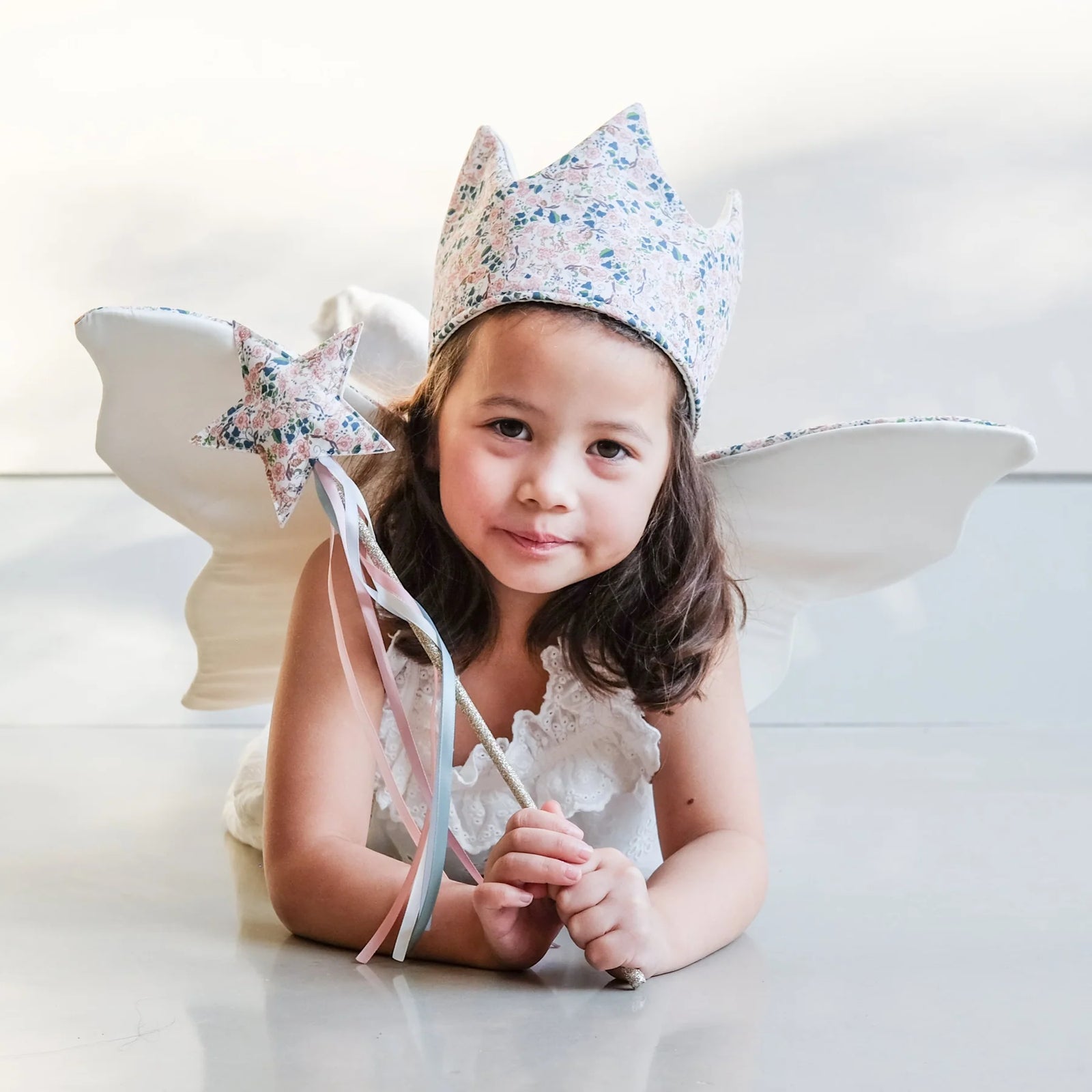 Child wearing floral fabric crown, holding a fabric wand laying on a white surface