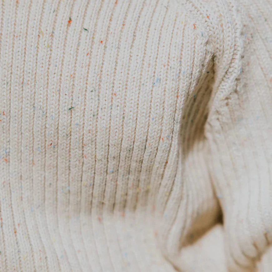 Close-up of a beige knitted sweater with speckled yarn.