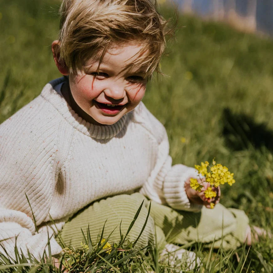 Child sitting in grass holding yellow flowers