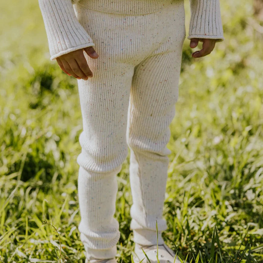 Person wearing a cream sweater and pants standing in a grassy field