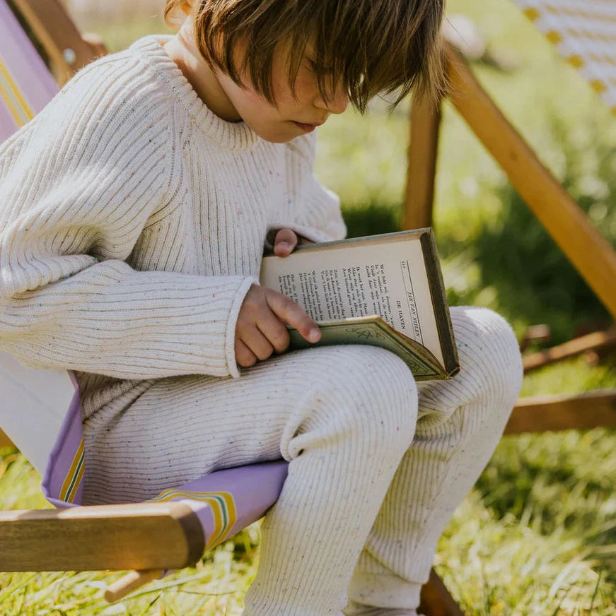 Child sitting outdoors on a bench, reading a book