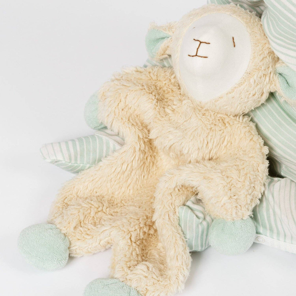 Plush toy sheep with a white face and green feet, held by a child wearing a striped pajama