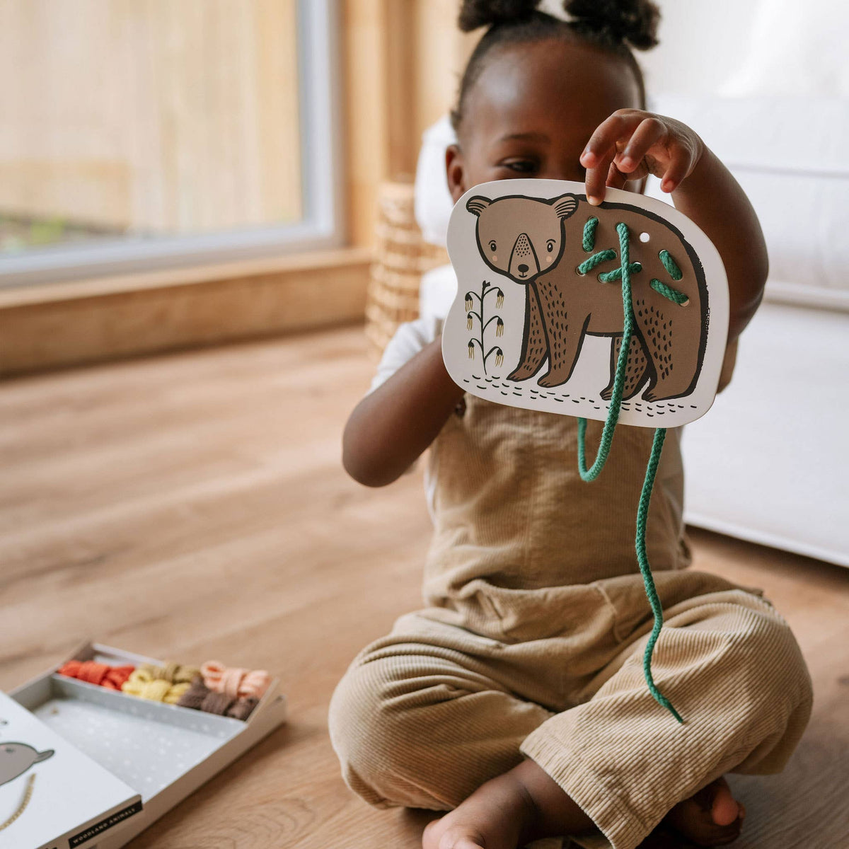 Child holding a bear mask with a wooden floor and books in the background