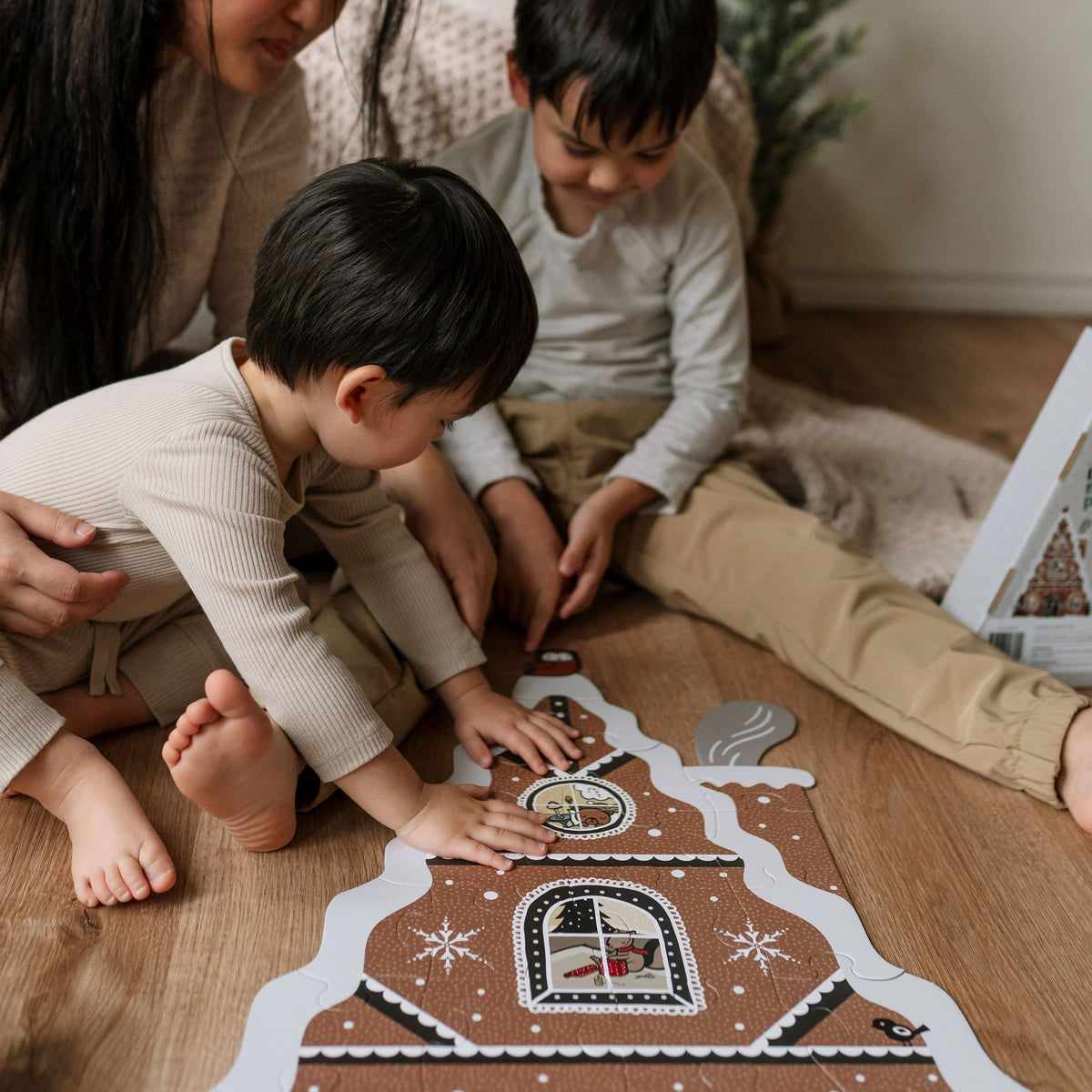 Two children and an adult sitting on the floor, engaged with a gingerbread house puzzle.