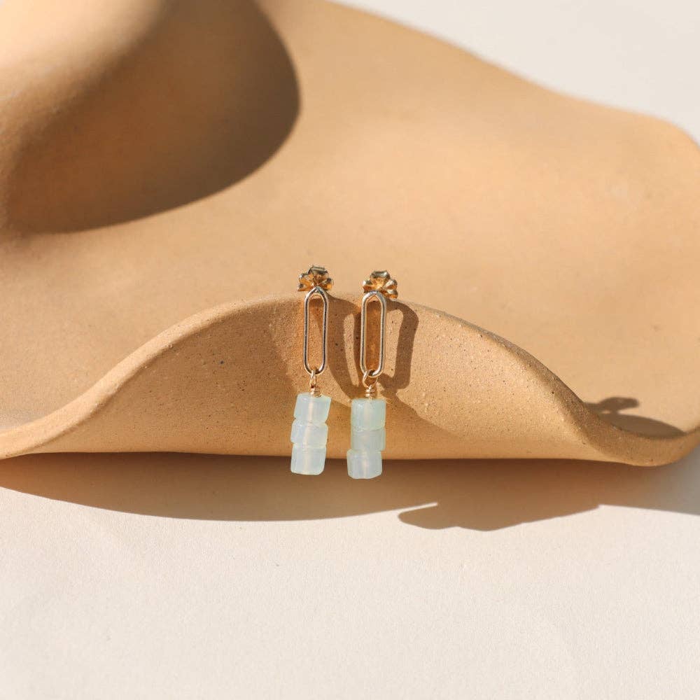 Gold earrings with clear stones on a beige surface