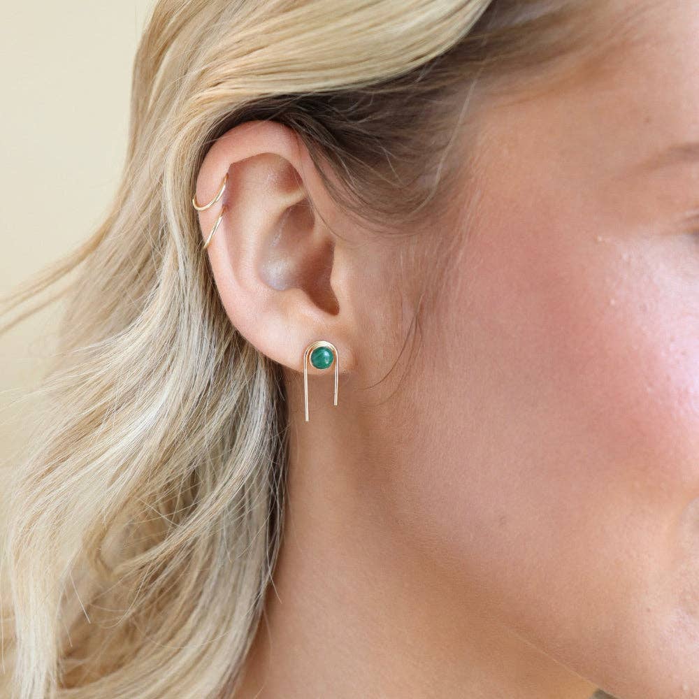 Gold earrings with green gemstones on a light background