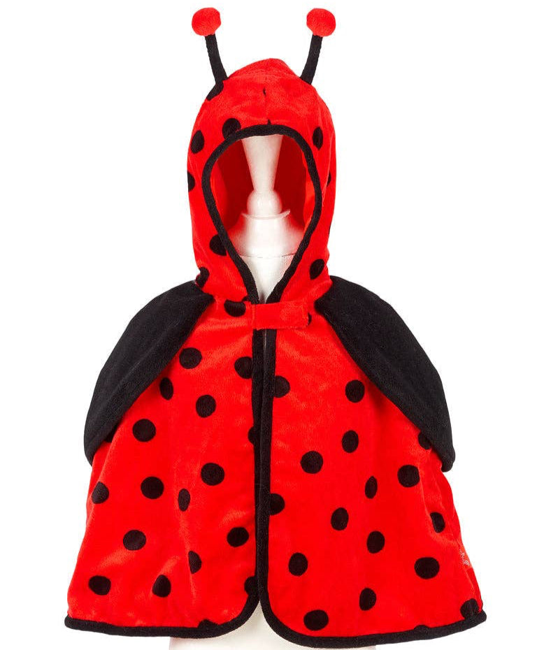 Child in a garden wearing a red and black outfit with polka dots, surrounded by greenery.