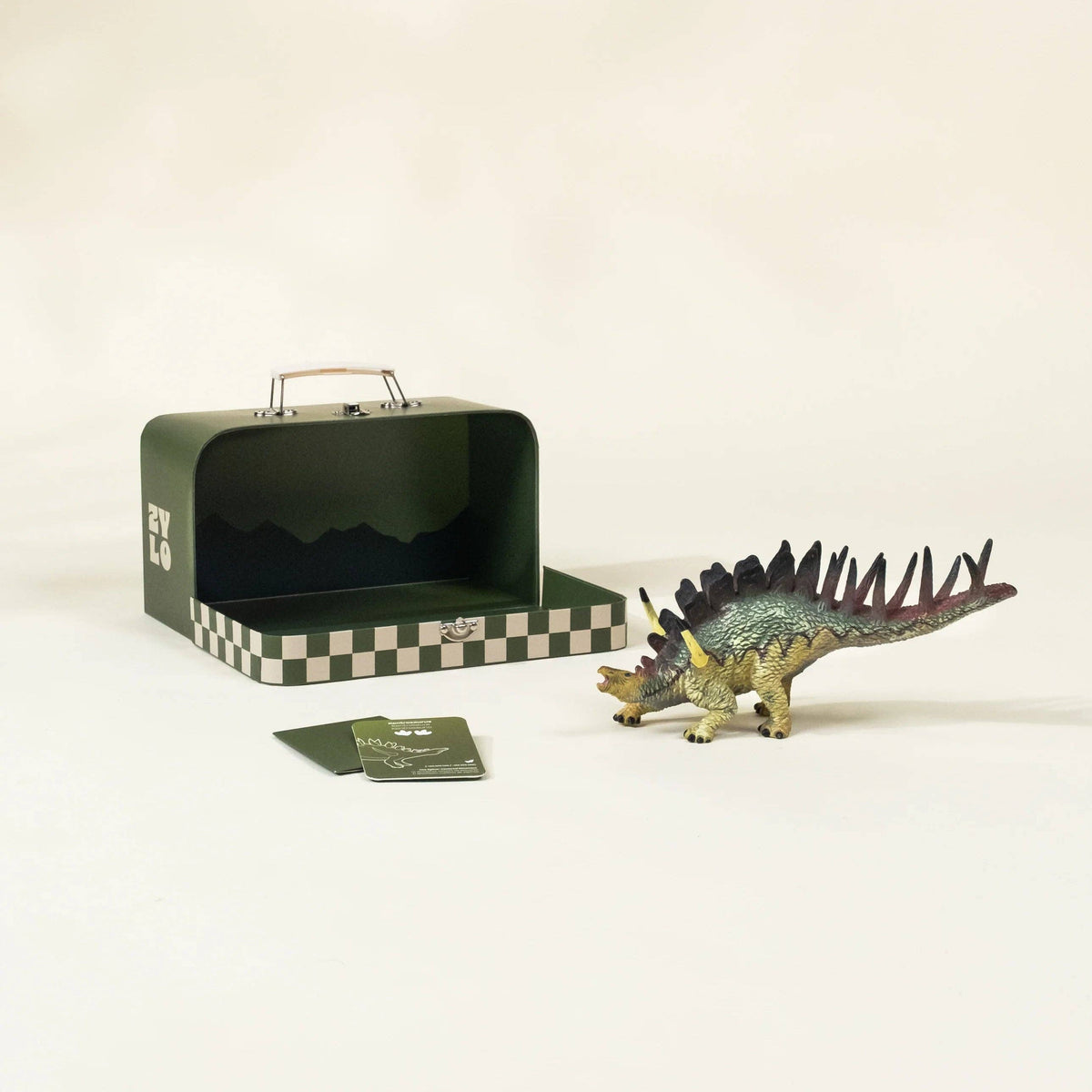 Dinosaur toy figure next to a green checkered suitcase on a white background