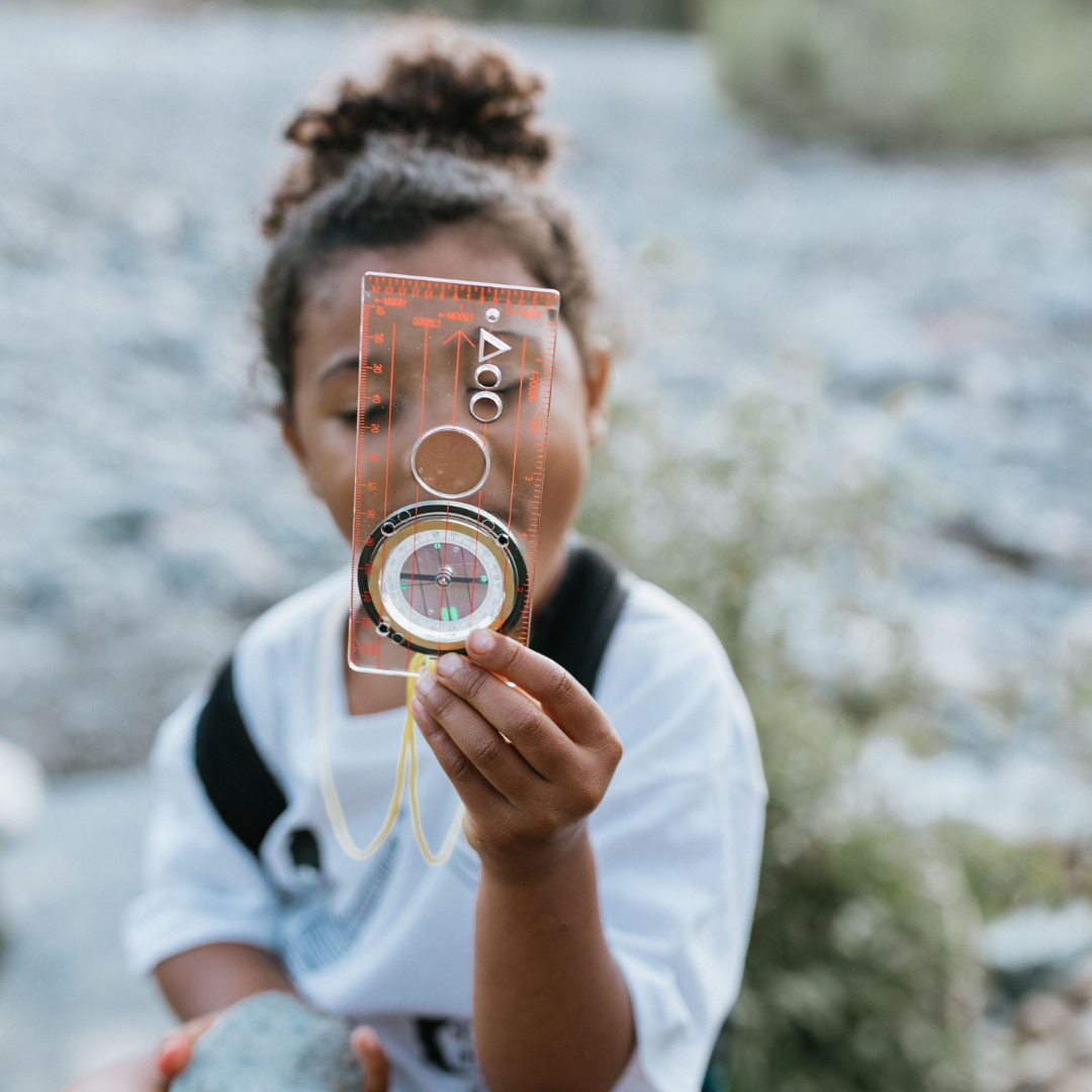 Child holding a transparent compass with a blurred natural background