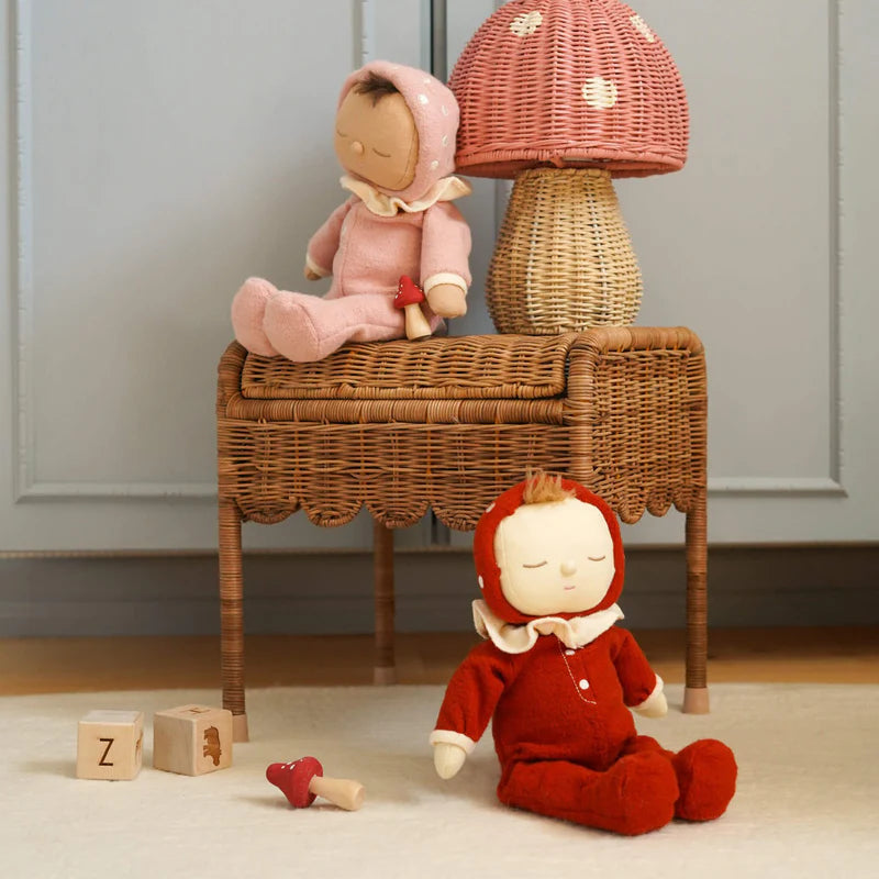 Two plush toys, one pink and one red, on a wicker stool and floor with wooden blocks.