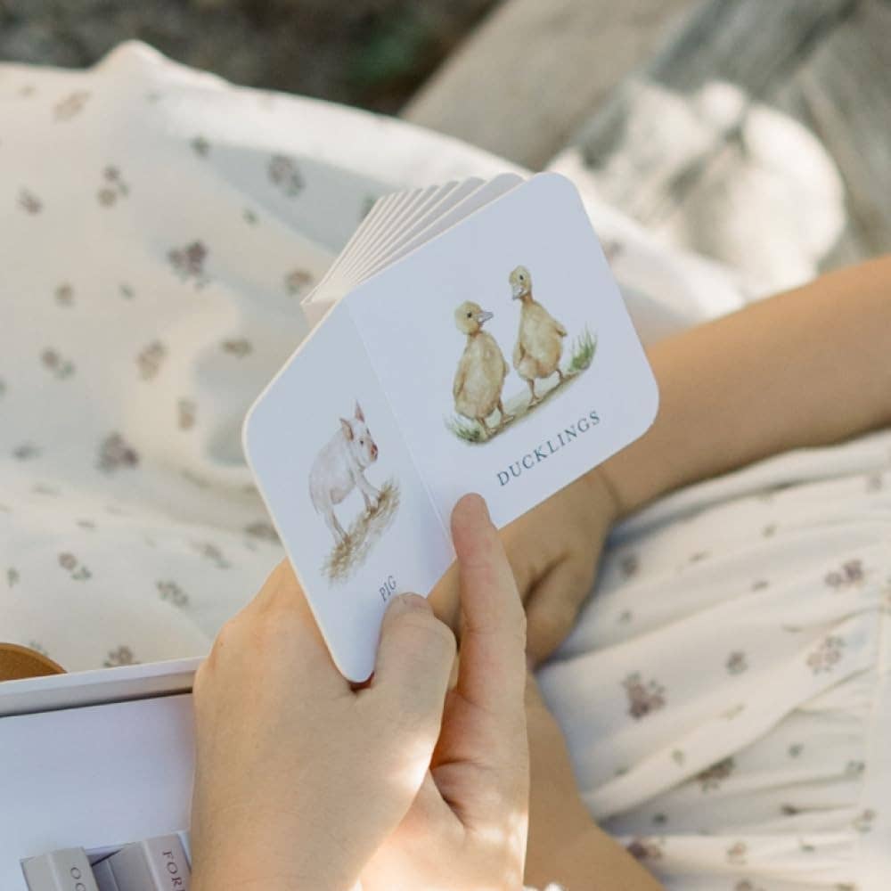 Hand holding a card with duckling illustration against a blurred natural background