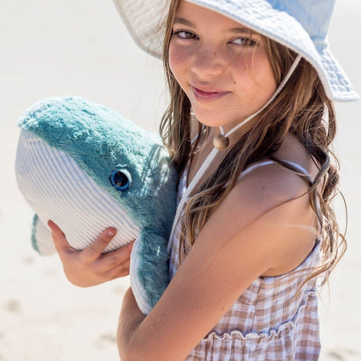 Young girl holding a plush shark toy on a beach