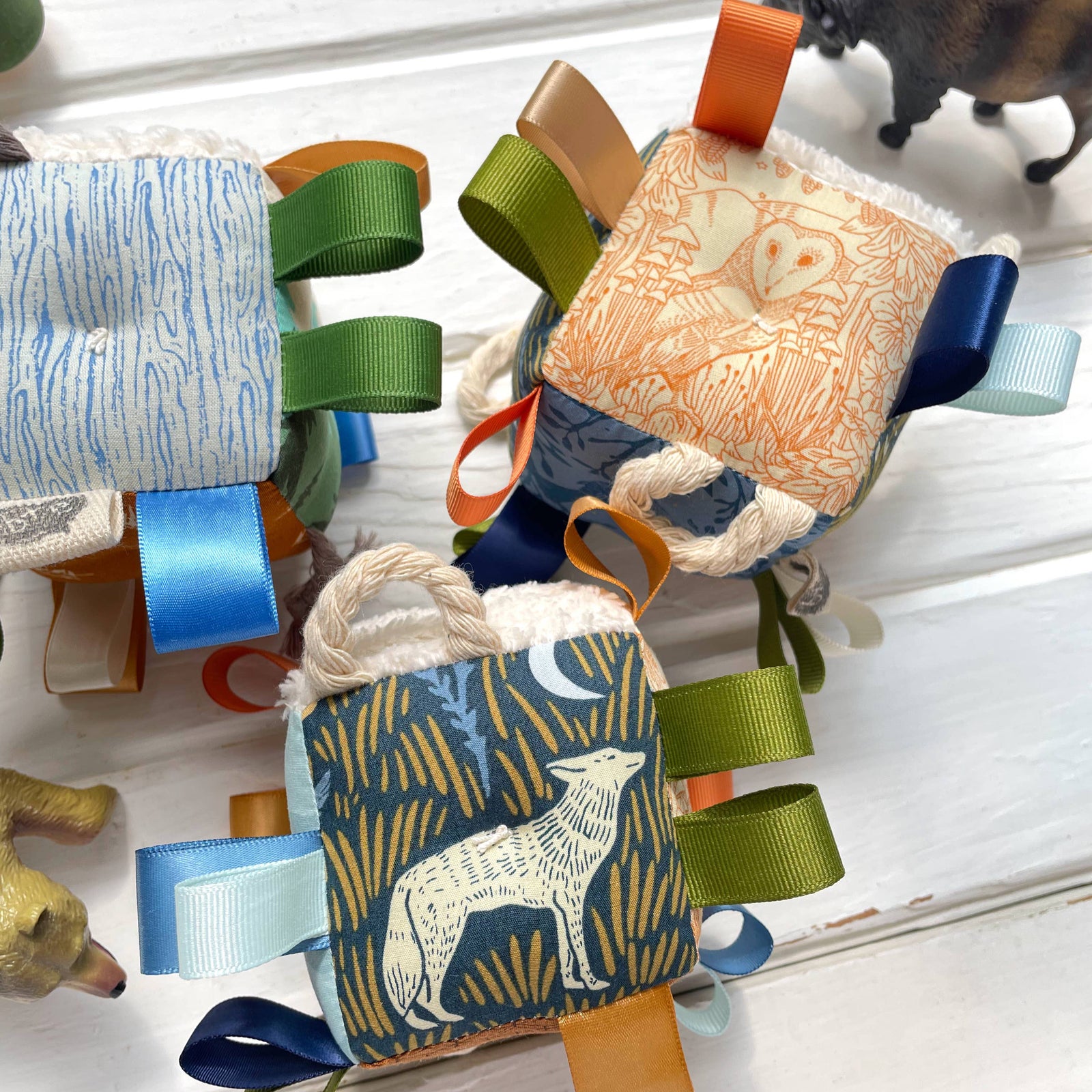 A baby sensory taggie block featuring a wolf design in blue, gold, and green fabrics with ribbons and a rattle.